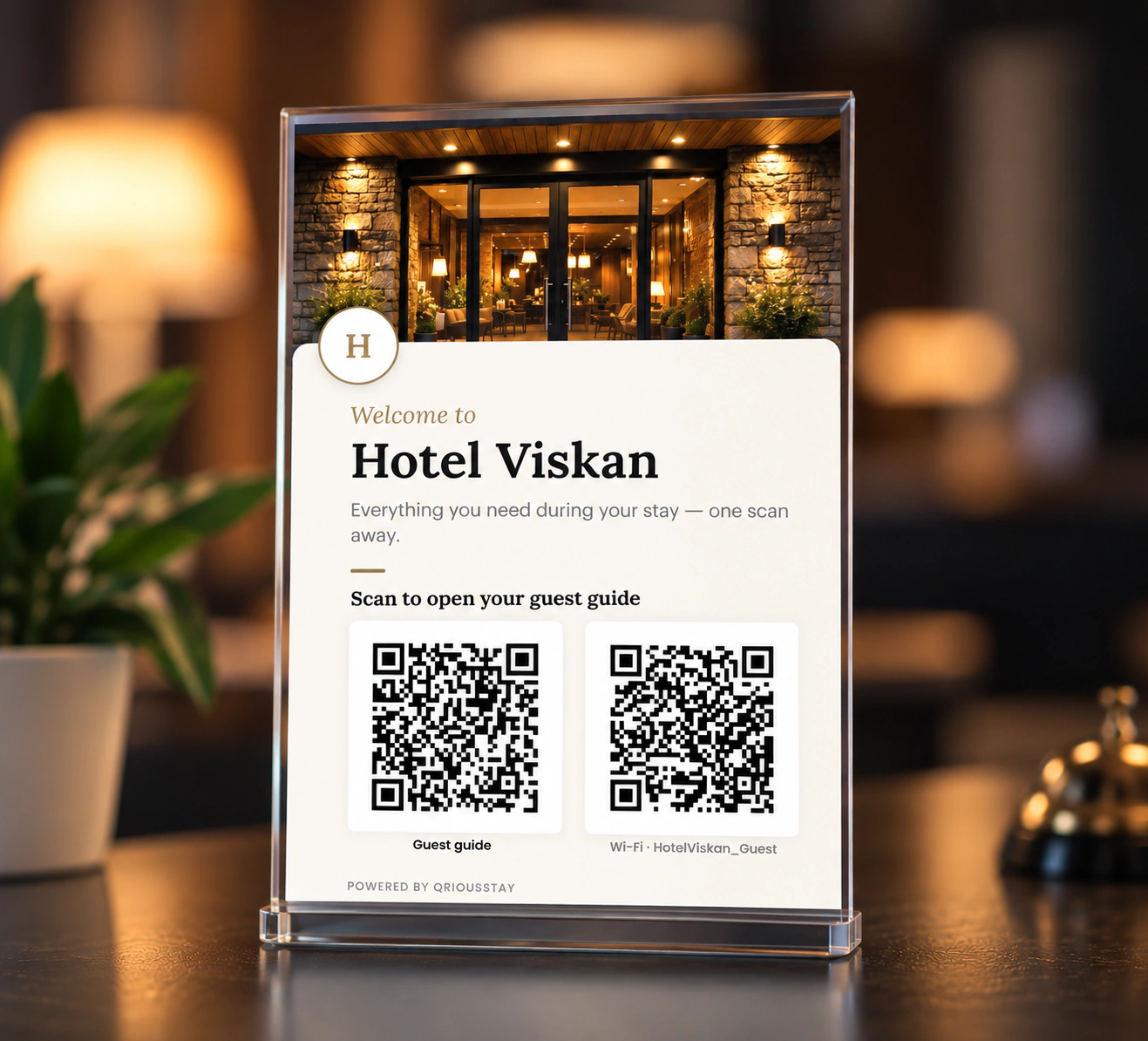 Ein gedrucktes QRiousStay-Schild in einem transparenten Ständer auf einem Hotelempfangstresen, mit einem Guide-Code und einem WLAN-Code.